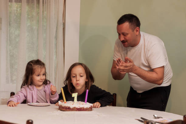 Child blowing birthday candle at home Girl blowing birthday candle whit her father and sister in living room birthday wishes for daughter stock pictures, royalty-free photos & images