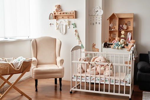 Scandinavian style white interior children's room, bedroom, nursery. Baby cot with canopy. Wooden shelves and toys