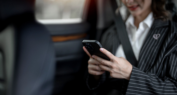 Young businesswoman using the mobile phone while sitting in the back seat in a passenger car.