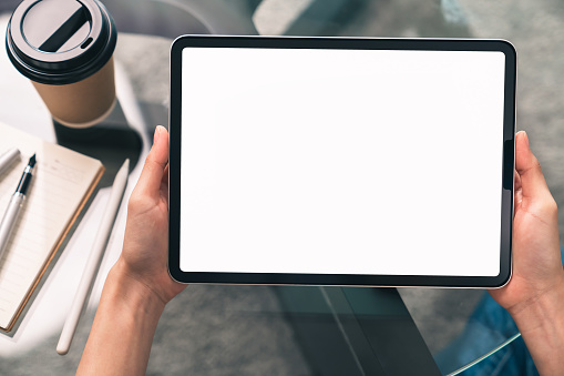 Woman hand holding digital tablet and sitting on the table in the house, mock-up of a blank screen for the application.