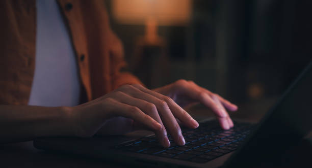 Woman using laptop and hand typing on the computer keyboard in the office at night. stock photo