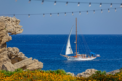 Beautiful sail boat passing near rocks and flowers in Rhodes Greece