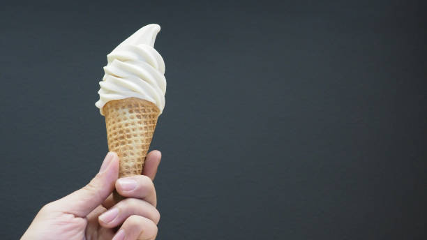 istock The hand is holding a soft-serve ice cream cone with a black background. 1420399119