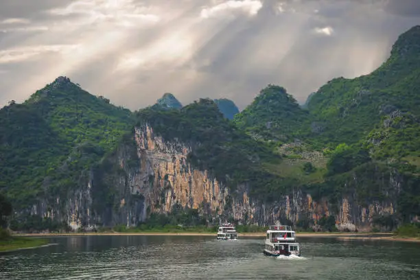 Sightseeing boats carrying tourists sailing among high vertical cliffs of karst mountains on the magnificent Li river flowing between Guilin and Yangshuo towns, China