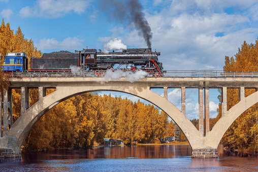 Retro steam train moves above the river at autumn day.