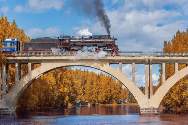 Retro steam train moves above the river at autumn day.