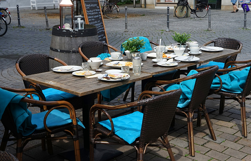 A restaurant table to be cleared. The guests have left. The photo was taken in Germany. The dishes described on the plate behind the table are therefore in German