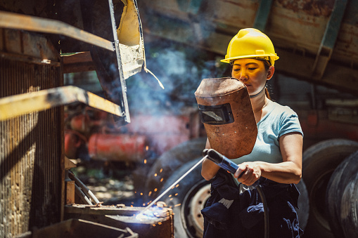 Close-up of an Asian Chinese Female Industrial Welder holding welding Torch with welding sparks at construction site.