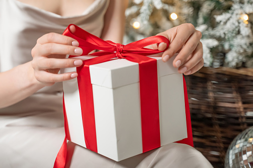 Box with holiday gifts. Merry Christmas and Happy New Year white gift box with red bow in woman hands