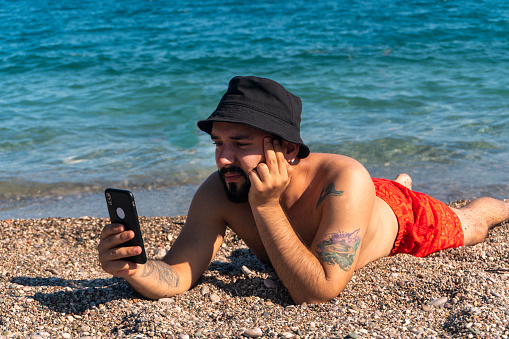Man spending time with his phone on the beach during summer vacation on a summer day