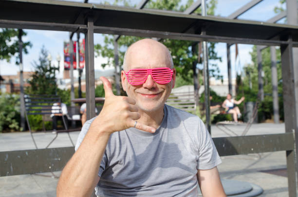 Smiling looking up young caucasian man with sunglasses in a white t-shirt on park with blurred sunny background. Selective focus. Portrait of a 32 year old young man.