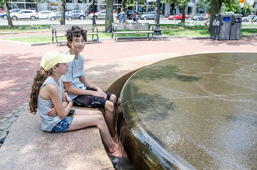 Two teenagers refreshing their feet in fountain in Boston during summer hot day