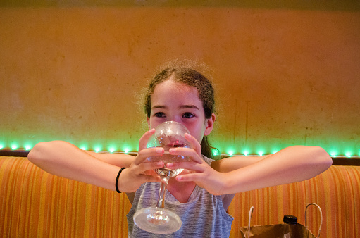 Teenager girl drinking water in wine glass in a restaurant