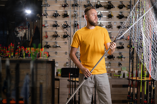 Man chooses fishing rod and landing net in the sports shop