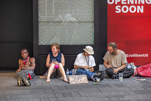 Manhattan, New York, NY, USA - July 10th 2022: Four homeless people sitting on the sidewalk protesting against Covid-19 and begging for money