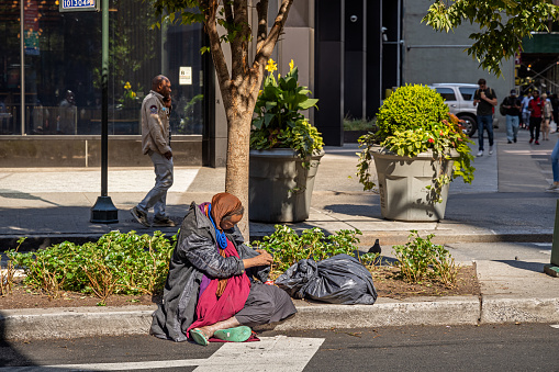 Manhattan, New York, NY, USA - July 10th 2022: Homeless African-American woman on a street corner at Broadway and West 31st Street with her belongings in a black plastic bag