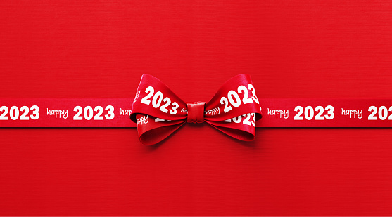 Happy 2023 written red tied bow ribbon sitting over red background. Horizontal composition with copy space. Happy 2023 concept.