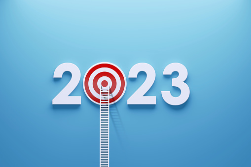 White ladder leaning on a red bull's eye target and 2023 written by white numbers on blue wall. Horizontal composition with copy space. 2023 resolutions concept.