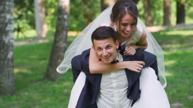 Newlyweds walk in the park. Bride Groom straddled like a horse. Slow motion
