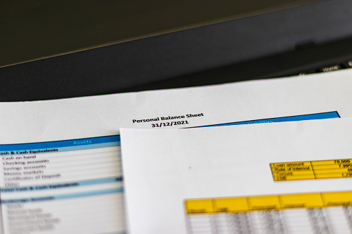 Close up shot of a print outs of excel table of a bank loan amortization table, personal balance sheet and laptop