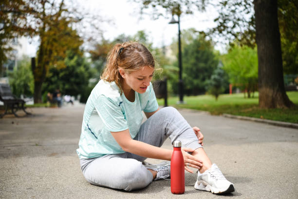 woman in pain sitting on the ground after twisting her ankle while jogging - twisted ankle imagens e fotografias de stock