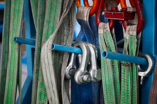 Different rigging equipment with dirty colorful strops hangs on metal rack in light warehouse of production plant close view