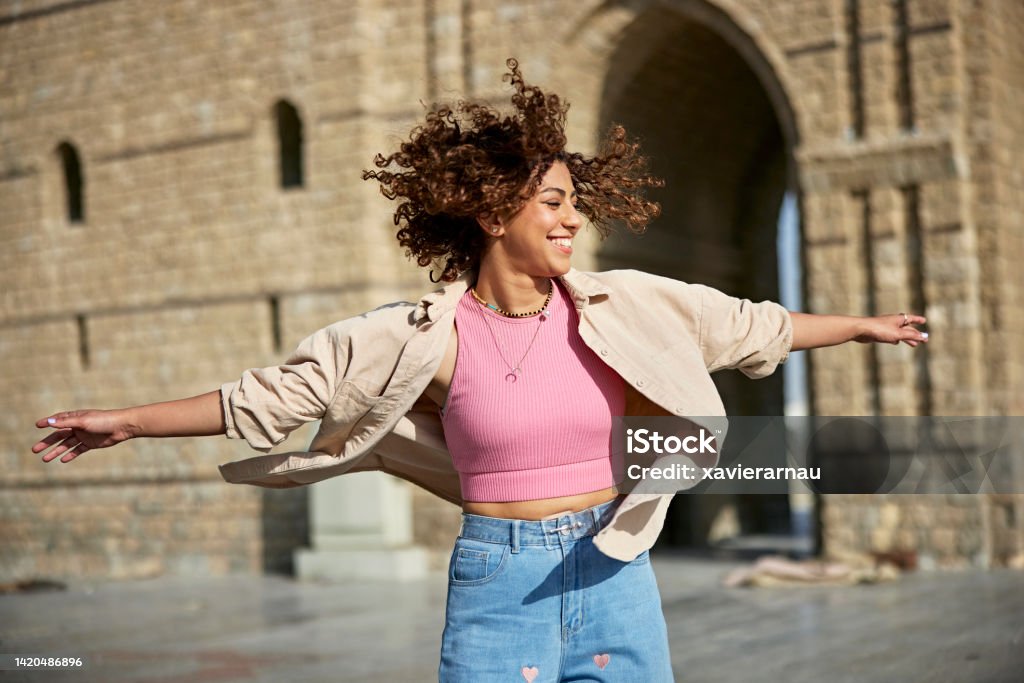 Carefree young woman twirling at Baab Makkah, Jeddah Front view of Middle Eastern woman in casual attire laughing while playing at historical landmark, the start of the road leading to Mecca. Saudi Arabia Stock Photo