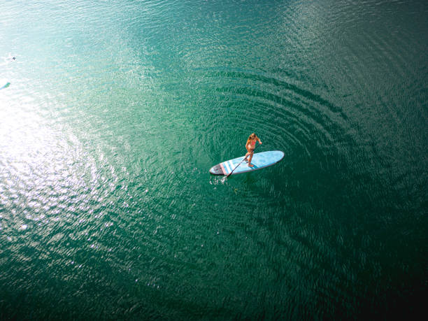 Aerial view of a woman exercising on a stand up paddle board Female relaxing on a large lake while paddling a stand-up paddle board.
Drone aerial view of lake and its calm waters. Beginner trying to learn and balance without falling. travel destinations 20s adult adventure stock pictures, royalty-free photos & images