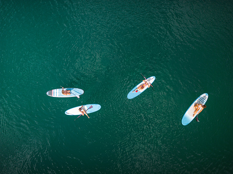 A group of women relaxing on a large lake while paddling a stand-up paddle board.
Drone aerial view of lake and its calm waters. All beginners trying to learn and balance themselves without falling.