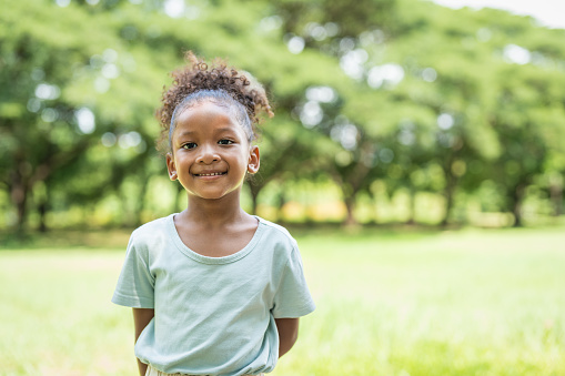 Portrait of a little girl with curly hair smiling looking at camera.Kid girl standing in the park.