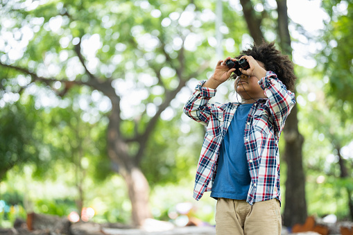 African American little boy with binoculars telescope looking birds in park on holidays in summer