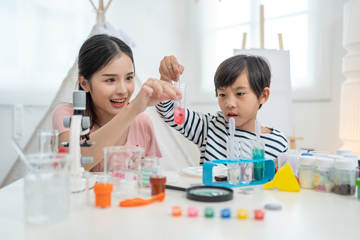 Asian mother and little boy making chemical experiments and tests in living room at home.Home laboratory education science concept for kids.