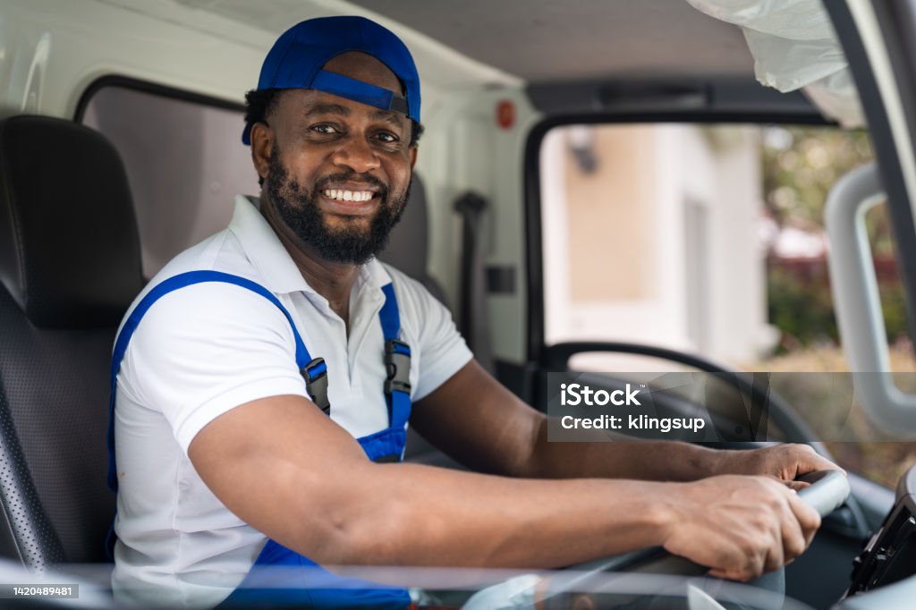 Smiling professional man mover worker in blue uniform driving truck to delivery and moving house service Delivery Person Stock Photo