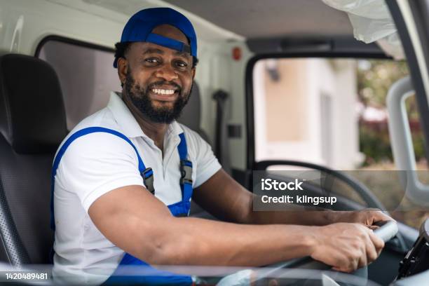 Smiling Professional Man Mover Worker In Blue Uniform Driving Truck To Delivery And Moving House Service Stock Photo - Download Image Now