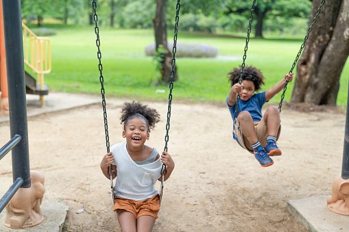 Happy African American little girl and boy have fun at the playground in the park