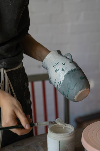 istock Female artisan in apron creates ceramic tableware painting white vase with brush in workshop 1420491187