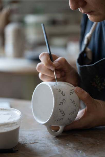 istock Woman draws pattern with dark paint on white ceramic mug using brush on blurred background 1420491251