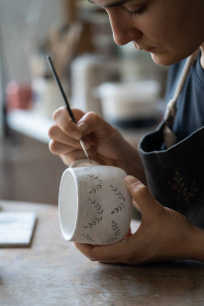 istock Woman draws pattern with dark paint on white ceramic mug using brush on blurred background 1420491255