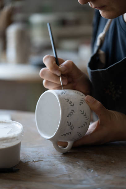 istock Woman draws pattern with dark paint on white ceramic mug using brush on blurred background 1420491261