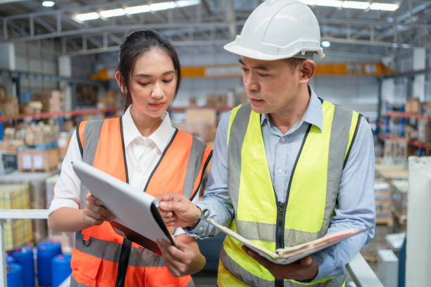 istock Male inventory manager holding notebook explaining products information in paper on clipboards with female worker in warehouse 1420492906