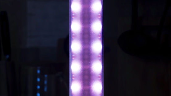Purple color led strip light shining in the dark room. Close up of lilac glowing vertical narrow lamp, colorful illumination of the room.