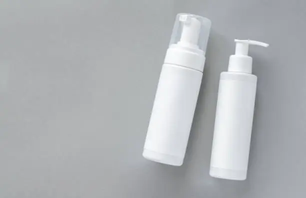 Mock-up of white plastic cosmetics bottles with skin care product on gray background. Top view