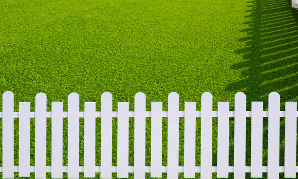 istock Sunlight and shadow on surface of white wooden picket on green artificial turf in front yard area 1420503296