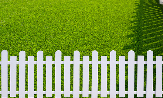Sunlight and shadow on surface of white wooden picket on green artificial turf in front yard area