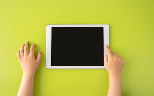 High angle shot of a little kid using a digital tablet with tablet computer on green background in horizontal with copy space.