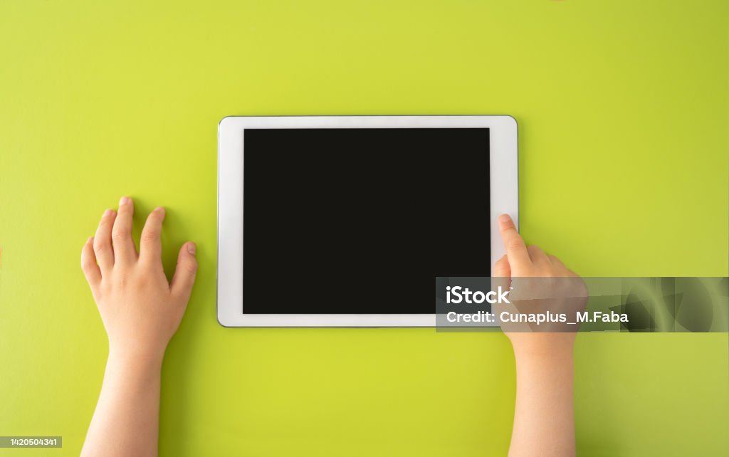 High angle shot of a little kid using a digital tablet High angle shot of a little kid using a digital tablet with tablet computer on green background in horizontal with copy space. Child Stock Photo