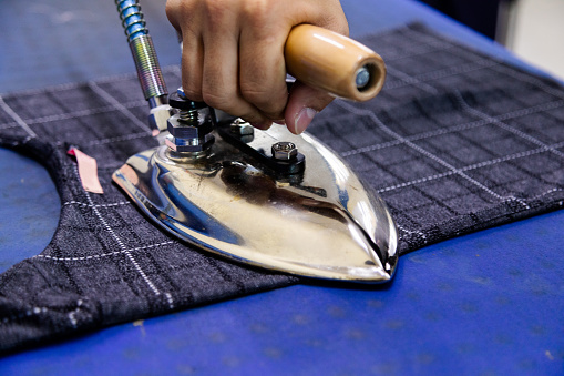 Tailor ironing clothes in tailoring shop with steam Iron