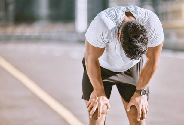 uomo stanco che riposa dopo la corsa di fitness, si prende una pausa dall'allenamento cardio e fa esercizi di benessere sulla strada nella città urbana. sportivo esausto e in forma che fa allenamento di routine in strada - exhaustion foto e immagini stock