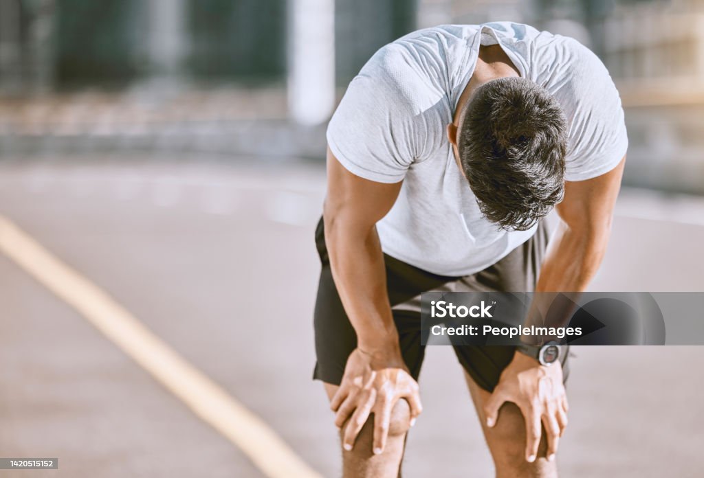 Tired man resting after fitness run, taking a break from cardio training and doing wellness exercise on the road in the urban city. Exhausted and fit sports person doing routine workout in street Tired Stock Photo