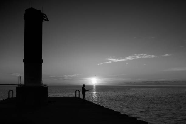 Manitowoc, Wisconsin, USA - July 22, 2022: The silhouette of a man fishing at sunrise from the south pier on Lake Michigan.